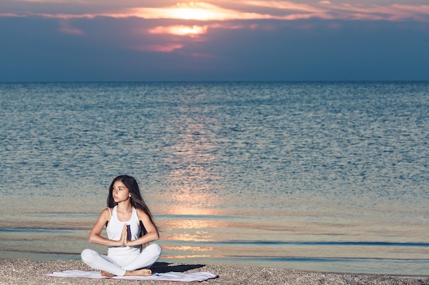 Niña haciendo yoga o meditación al amanecer en la playa