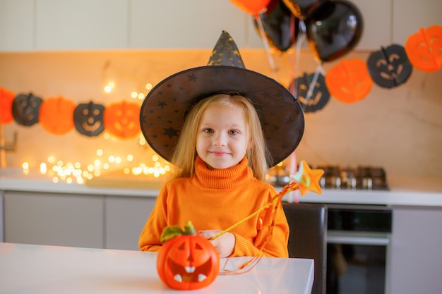 Niña en Halloween en un disfraz de bruja con una calabaza en casa en la cocina
