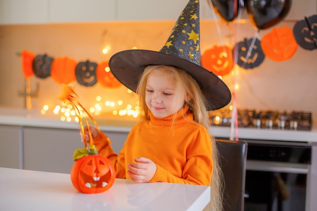 Niña en Halloween en un disfraz de bruja con una calabaza en casa en la cocina