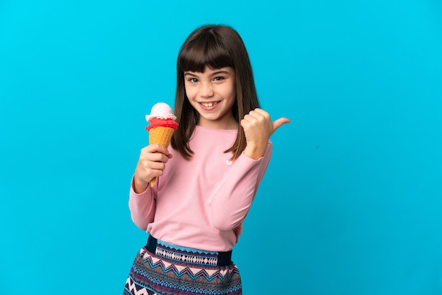 Niña con un helado de cucurucho aislado en la pared azul apuntando hacia el lado para presentar un producto