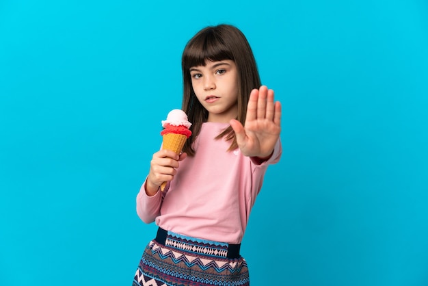 Niña con un helado de cucurucho aislado en la pared azul haciendo gesto de parada