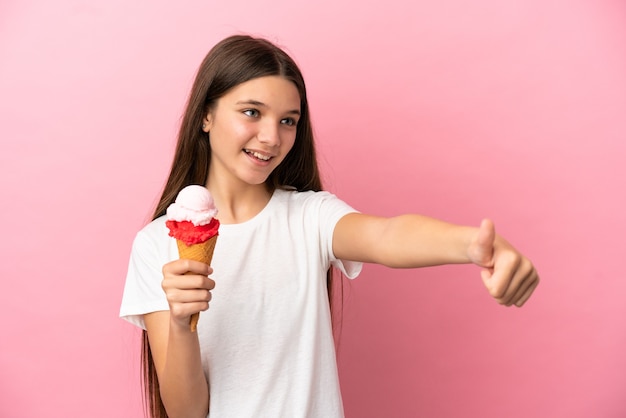 Niña con un helado de cucurucho sobre fondo rosa aislado dando un gesto de pulgar hacia arriba