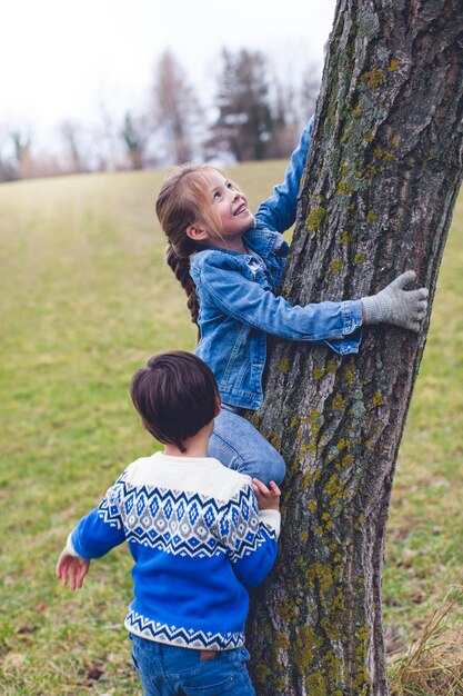 Foto niña con hermano trepando a un árbol en el campo