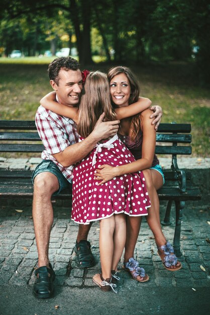 Una niña hermosa abrazó a sus padres en el parque.