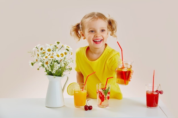 Una niña hermosa alegre con una camiseta amarilla con varios refrescos y cócteles de bayas.