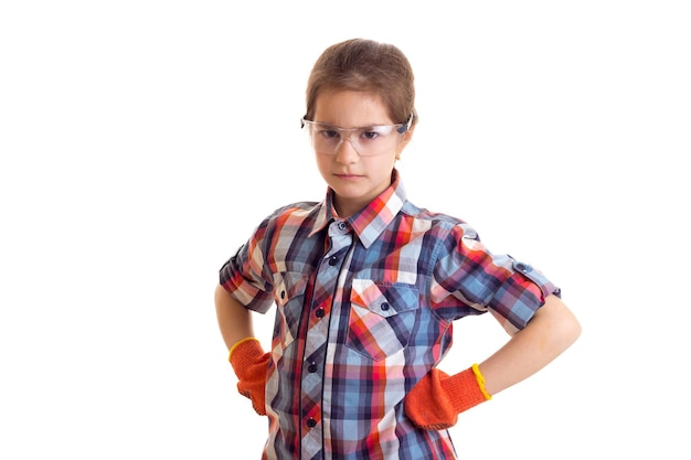 Niña hermosa en camisa a cuadros con guantes y gafas sosteniendo el nivel del edificio en el estudio