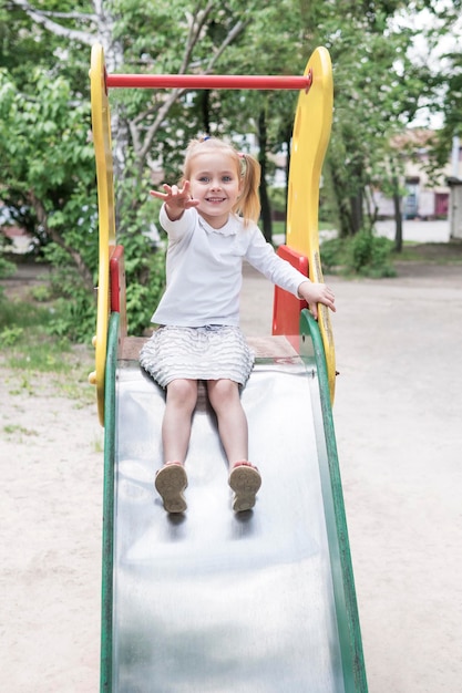 Una niña hermosa estira su mano mientras se sienta en un tobogán para niños