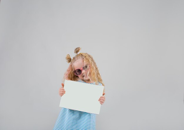 Foto una niña hermosa con gafas rubias sostiene una sábana blanca sobre un fondo blanco en sus manos