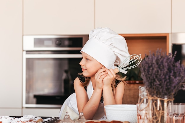 Una niña hermosa con un gorro de cocinero blanco en la cocina.