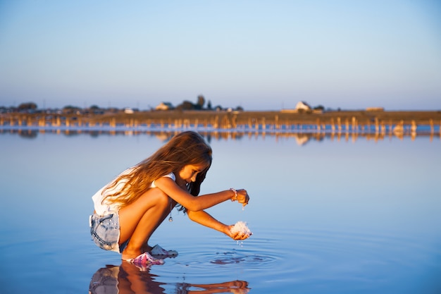 Una niña hermosa con un hermoso cabello suelto mira la sal en un esmalte acuoso transparente sobre un fondo transparente