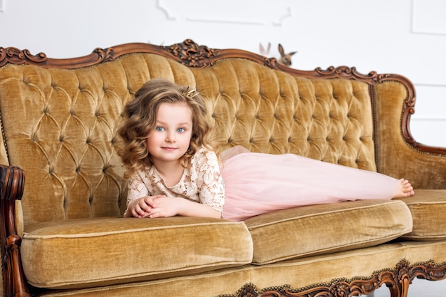 Niña hermosa y linda con un vestido de fiesta de moda en un lujoso sofá vintage