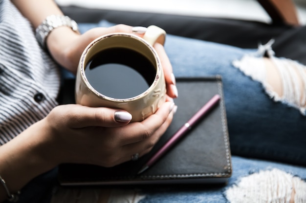 Foto una niña con una hermosa manicura sostiene un libro con una taza de café. estilo de moda