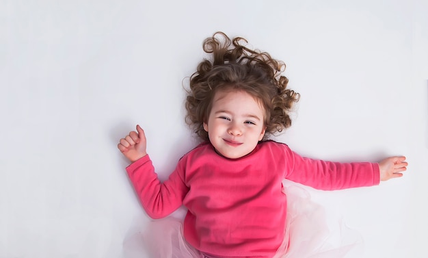 La niña hermosa miente en el piso blanco y la sonrisa. El concepto de una infancia feliz.