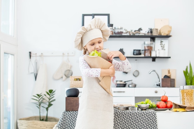 Niña hermosa niña cocinar en la cocina con diferentes verduras y espaguetis