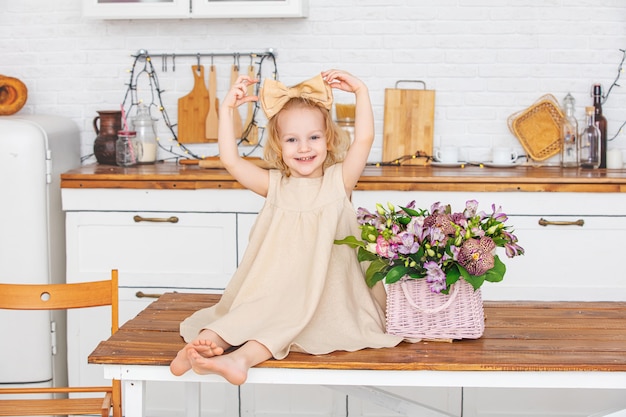 Niña hermosa niña con flores en la cocina en casa