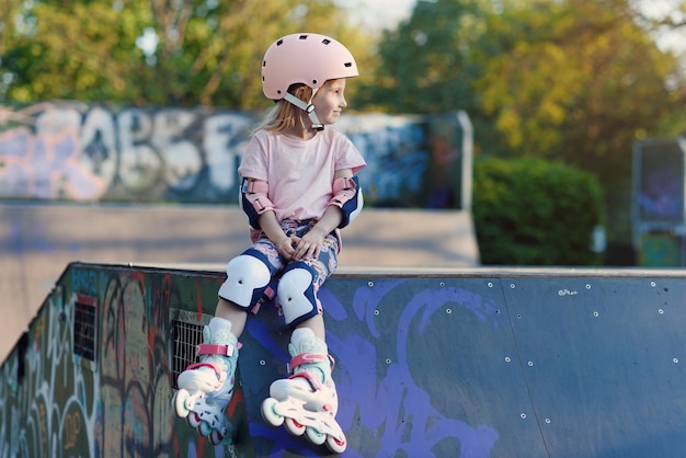 Niña hermosa en patines en un casco y protección de manos y pies en un parque de patinaje