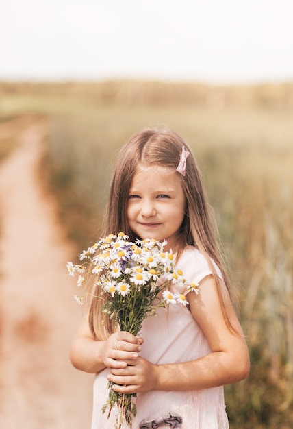 Una niña hermosa con un ramo de margaritas en un campo de trigo