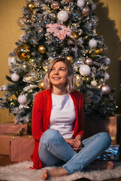 Foto niña hermosa sentada cerca del árbol de navidad