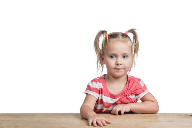 Niña hermosa sentada en una mesa de madera aislada en un fondo blanco