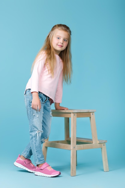 Niña hermosa en suéter rosa y jeans posando en el estudio