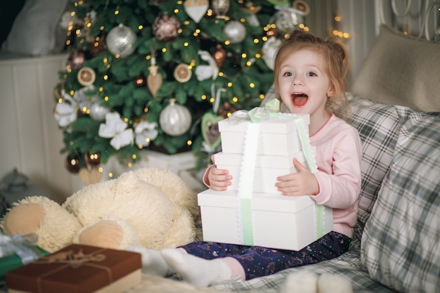 Niña hermosa con sus regalos se sienta en su cama