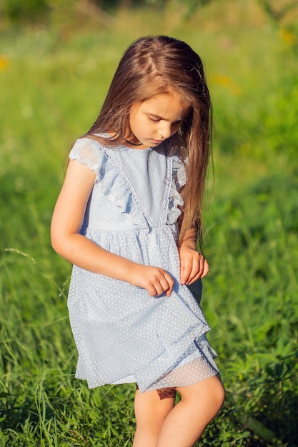 Foto niña hermosa con un vestido azul descalza en verano en la calle