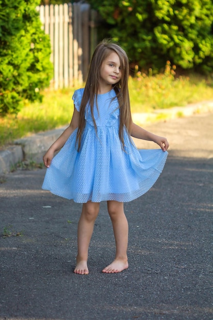 Foto niña hermosa con un vestido azul descalzo en verano en la calle2