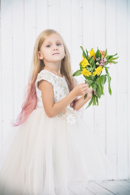 Niña hermosa en vestido hermoso con ramo de flores sobre fondo blanco de madera