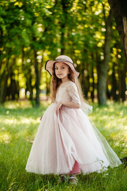 Una niña hermosa en un vestido y un sombrero en el parque sonríe.