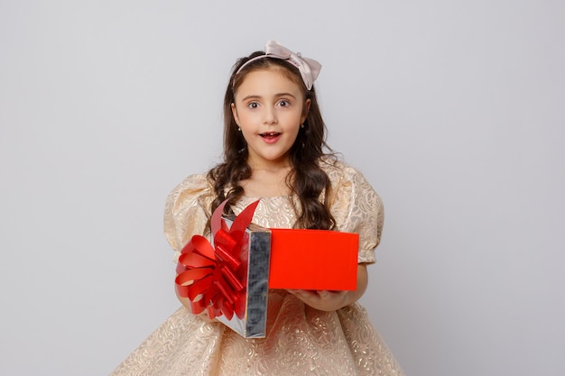 Una niña con un hermoso vestido sostiene una caja de regalo sobre un fondo blanco.