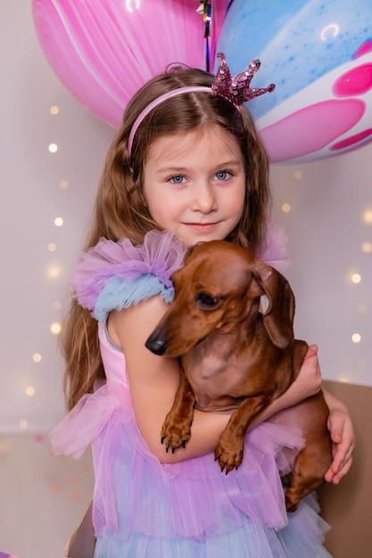 Niña con un hermoso vestido sostiene un perro salchicha enano en sus brazos mascota favorita