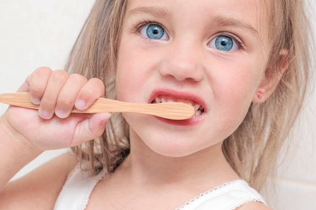 Foto niña con hermosos ojos azules se cepilla los dientes con un cepillo de dientes de bambú. closeup retrato