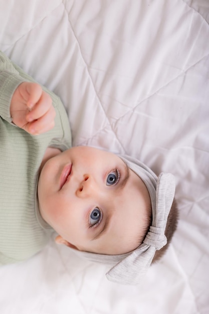 Una niña con hermosos ojos grandes está frotando al bebé en casa en la cama con un traje de algodón sobre ropa de cama blanca