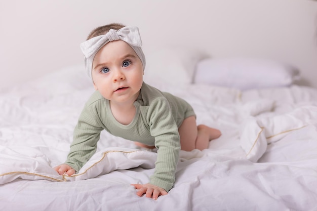 Una niña con hermosos ojos grandes está frotando al bebé en casa en la cama con un traje de algodón sobre ropa de cama blanca