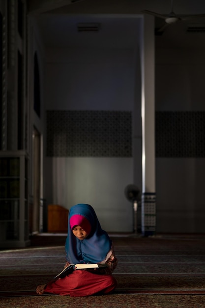 Niña con hijab leyendo un libro mientras está sentada en la mezquita
