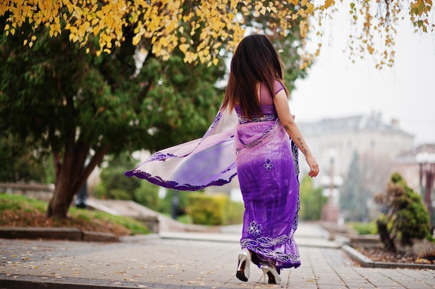 Niña hindú india en sari violeta tradicional posada en la calle otoño