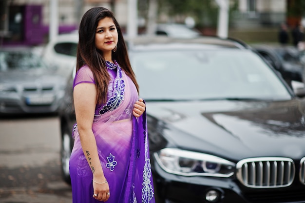 Niña hindú india en sari violeta tradicional posó en la calle contra suv coche negro.