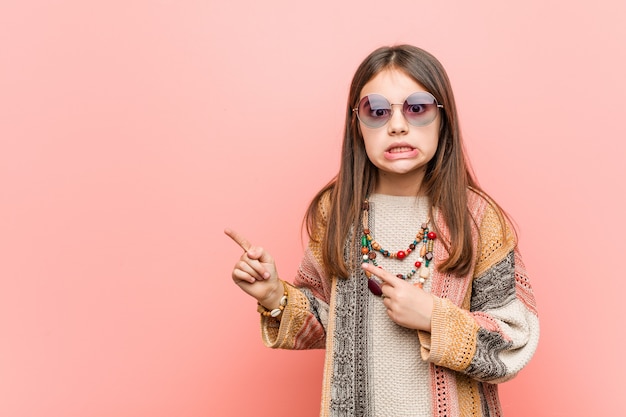 Niña hippie sorprendida señalando con los dedos índices a un espacio en blanco.