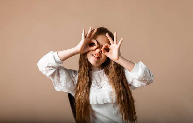 Una niña hizo sus manos con gafas en los ojos en el parque. Feliz niña de 12 años se sienta en el césped del parque y hace vasos con las manos