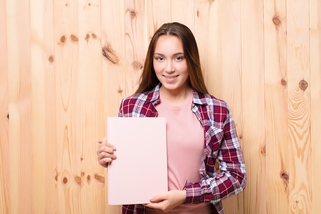 Niña con una hoja de papel contra la pared de madera