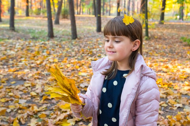 Niña con hojas de arce juega en el parque de otoño Concepto de infancia feliz