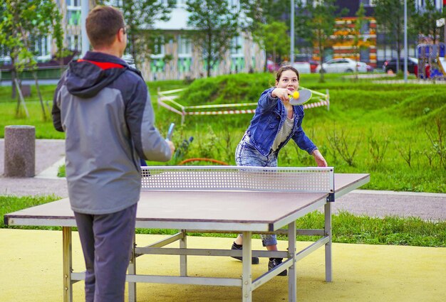 Una niña y un hombre juegan al tenis de mesa en el patio de un edificio alto