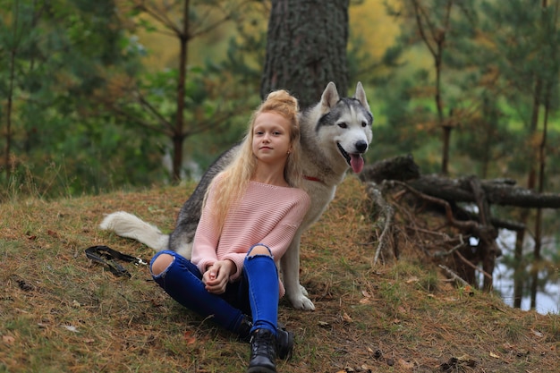 Una niña con un husky camina en el bosque.