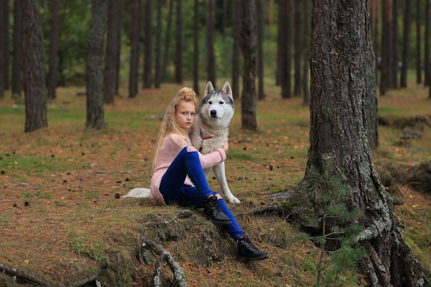 Una niña con un husky camina en el bosque.