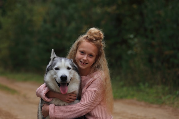 Una niña con un husky camina en el bosque.