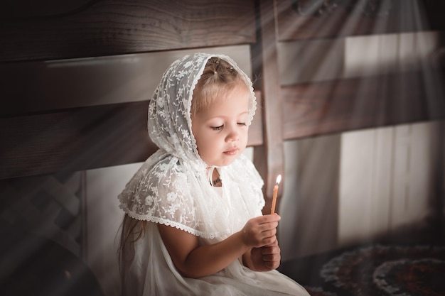 Una niña en una iglesia o iglesia con una vela en las manos reza al ícono o vino a adorar en la iglesia ortodoxa rusa