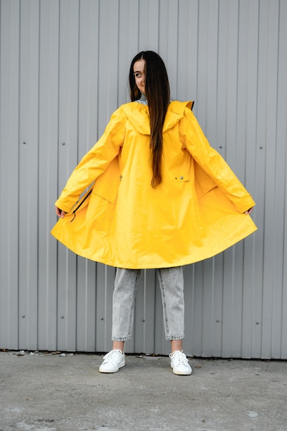 Niña con un impermeable amarillo y pantalones vaqueros grises se encuentra en un fondo gris de la subcultura juvenil