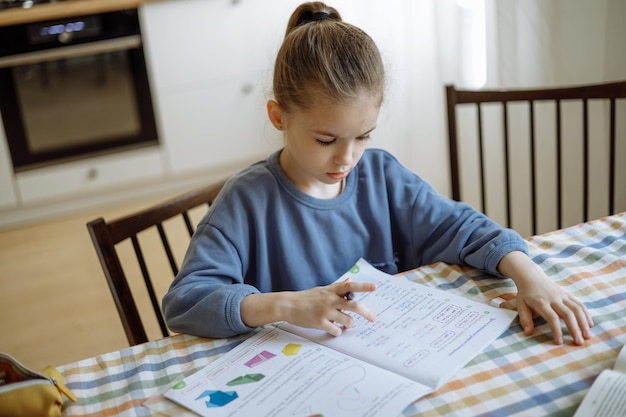 una niña independiente de 7 años haciendo su tarea escolar en casa en la cocina