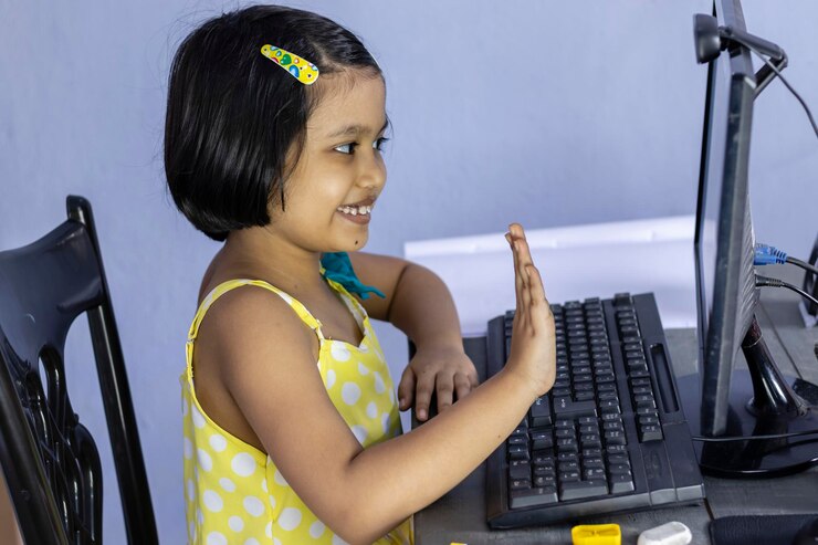 Foto una niña india con cara sonriente sentada frente a la computadora y agitando la mano hacia el monitor
