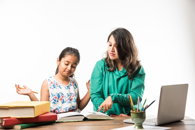 Foto niña india estudiando con la madre o el maestro en la mesa de estudio con computadora portátil, libros y divertirse aprendiendo